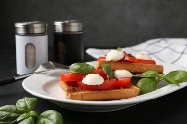 Mozarella peynirli, domatesli ve fesleğenli lezzetli sandviçler koyu renkli masada, yakın plan.