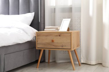 Yatağın yanında kitap ve çerçeve olan komodin.