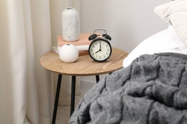 Yatağın yanında alarm saati ve dekorasyonu olan komodinin yanında.