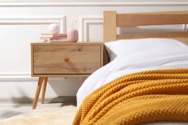 Yatağın yanında kitap ve dekor olan bir komodin.