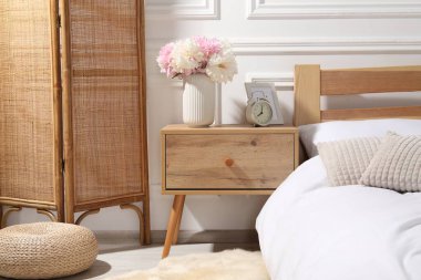 Komodinin yanında çalar saat ve yatağın yanında çiçekler var.