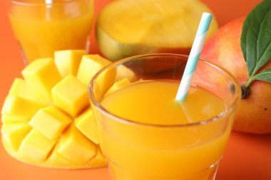 Bardakta lezzetli mango suyu ve turuncu arka planda taze meyve, yakın plan.