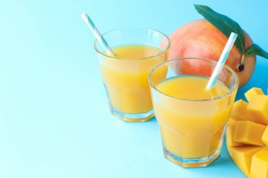 Bardakta lezzetli mango suyu ve açık mavi arka planda taze meyve, yakın plan. Metin için boşluk