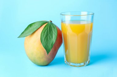 Bardakta lezzetli mango suyu ve açık mavi arka planda taze meyve.
