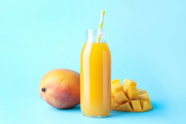 Cam şişede lezzetli mango suyu ve açık mavi arka planda taze meyve.
