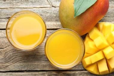 Bardakta lezzetli mango suyu ve ahşap masada taze meyveler.