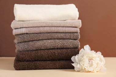 Kahverengi arka planda bej masa üzerinde havlu ve şakayık çiçeği yığını