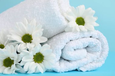 Açık mavi arka planda yumuşak havlular ve kasımpatı çiçekleri, yakın plan.