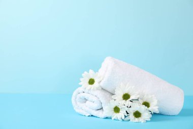 Açık mavi arkaplanda yumuşak havlular ve kasımpatı çiçekleri, metin için boşluk