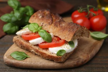 Mozarella peynirli, domatesli ve ahşap masadaki fesleğenli lezzetli sandviç.