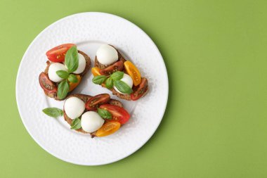 Mozarella peynirli lezzetli sandviçler, yeşil arka planda domates ve fesleğen, üst manzara. Metin için boşluk