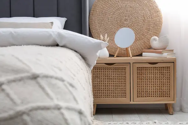 Yatağın yanında ayna, dekor ve kitap olan bir komodin.