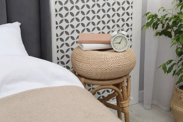 Çalar saati olan yan masa ve yatağın yanında kitaplar.