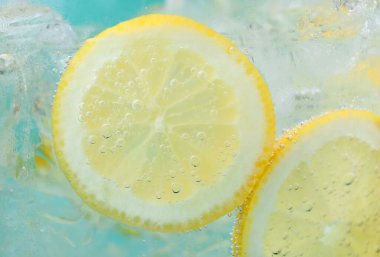Açık mavi arka planda limon dilimleri ve buzla soda tazeleniyor. Yakın plan.