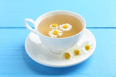 Fincanda nefis papatya çayı ve açık mavi ahşap masada taze çiçekler, yakın plan.