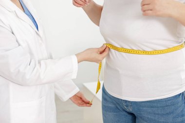 Kilo kaybı. Klinikte kilolu kadının belini bantla ölçen beslenme uzmanı.