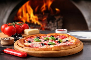 Fırına karşı gri masada taze pişmiş pizza ve malzemeler.