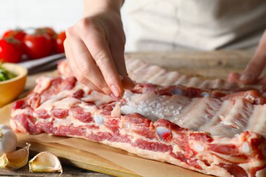 Kadın masadaki çiğ domuz pirzolasına deniz tuzu koyuyor.