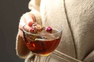 Gri arka planda cam bardakta aromatik bitki çayı olan kadın, yakın plan.