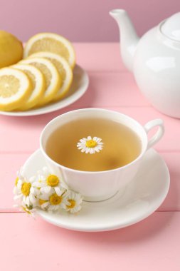 Fincanda nefis papatya çayı, taze çiçekler ve pembe ahşap masada limon, yakın plan.