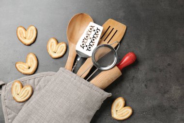 Fırın eldivenindeki farklı mutfak aletleri ve gri masadaki kurabiyeler.