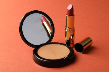 Aynalı açık yüz pudrası ve mercan zemininde ruj, yakın plan.