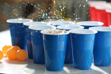 Alkolik içecekler plastik bardaktan sıçrıyor ve toplar açık tahta masada bulanık ışıklara karşı, yakın plan. Bira pong oyunu