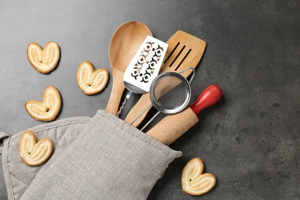 Fırın eldivenindeki farklı mutfak aletleri ve gri masadaki kurabiyeler.