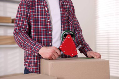 Karton kutuyu kapalı bir yere kapatmak için yapıştırıcılı bant kullanan bir adam.