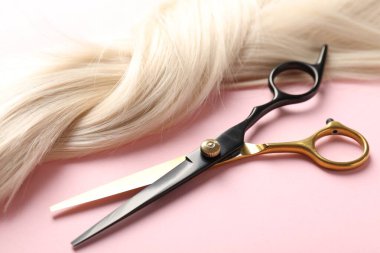 Açık pembe arka planda saç teli ve makas, yakın plan.