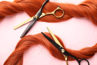 Açık pembe zemin üzerinde saç teli ve makas, üst görünüm