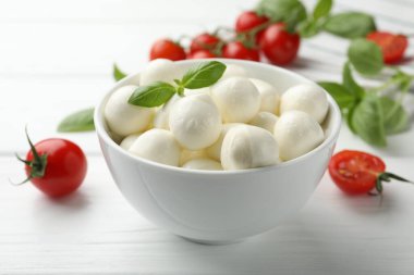 Lezzetli mozzarella peynir topları kasede fesleğen ve domatesler beyaz ahşap masada, yakın plan.