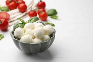 Lezzetli mozzarella peyniri topları, domates ve fesleğen beyaz ahşap masada, yakın plan. Metin için boşluk
