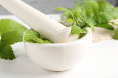 Taze limon merhemi yaprakları ve beyaz ahşap masada havan topuzu, yakın plan.