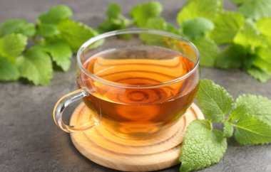 Cam bardakta Aromatik limon merhemi çayı ve gri desenli masada taze yapraklar, yakın plan.