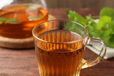 Cam fincanda aromatik limon merhemi çayı, çaydanlık ve ahşap masada taze yapraklar, yakın plan.