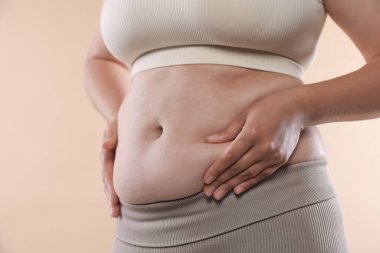 Bej arka planda aşırı göbek yağlı bir kadın, yakın plan. Aşırı kilolu