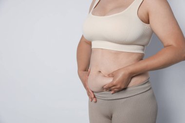 Hafif arka planda göbeği aşırı yağlı bir kadın, yakın plan ve mesaj için yer. Aşırı kilolu