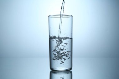 Ayna masasında açık gri gradyan arkaplana karşı cama su dökmek, yakın plan