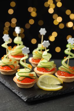 Siyah masadaki lezzetli kanepeler karanlık arka planda bulanık ışıklarla, yakın plan. Bokeh etkisi