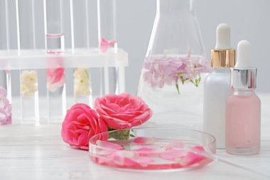 Lüks parfüm yapıyorum. Temel yağlar cam süslemede ve çiçekler beyaz ahşap masada, yakın plan.