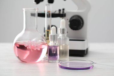 Lüks parfüm yapıyorum. Temel yağlar cam eşyalar, çiçekler ve mikroskop beyaz ahşap masa üzerinde, yakın çekim