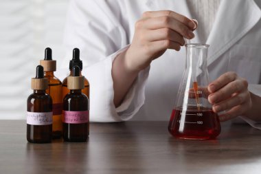 Laboratuardaki ahşap masada lüks parfüm üreten profesyonel parfümcü.