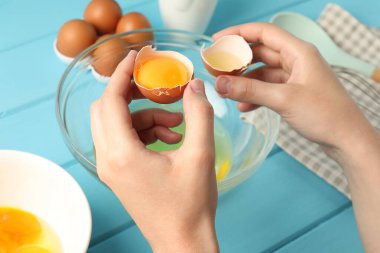 Açık mavi ahşap masada yumurta sarısını beyazdan ayıran kadın, yakın plan.