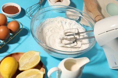 Açık mavi masada çırpılmış krema, yumurta ve diğer ürünlerle karıştırıcı, yakın plan.