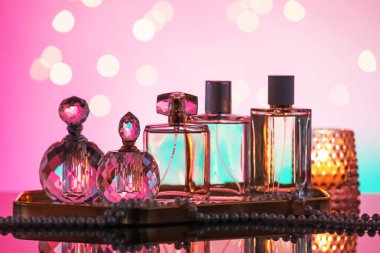 Ayna yüzeyinde birçok farklı parfüm şişesi ve aksesuar var. Pembe arka planda, bulanık ışıklar, yakın plan.