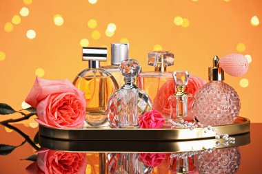 Farklı parfüm şişeleri ve çiçekler ayna yüzeyinde turuncu arka planda bulanık ışıklarla, yakın plan