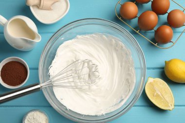 Açık mavi ahşap masada çırpılmış krema, yumurta ve diğer ürünlerle çırpın.