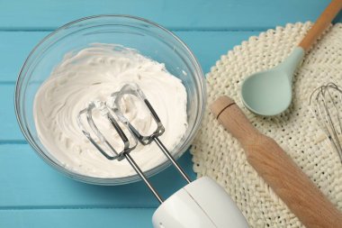 El çırpıcı, krem şanti kasede, merdane ve kaşık açık mavi ahşap masa üzerinde, yukarıda.