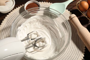 Masanın üstünde çırpılmış krema, yumurta ve diğer ürünlerle el çırpıcı var.